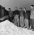 Lee Miller, Released prisoners in striped prison dress beside a heap of bones from bodies burne…